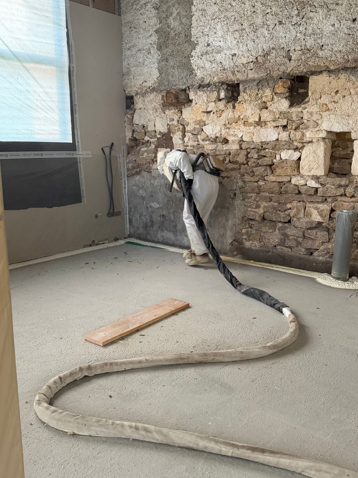 Applicateur Isolatech projetant la mousse polyuréthane sur mur en pierre apparente, charpente bois — chantier Pérouse, Territoire de Belfort