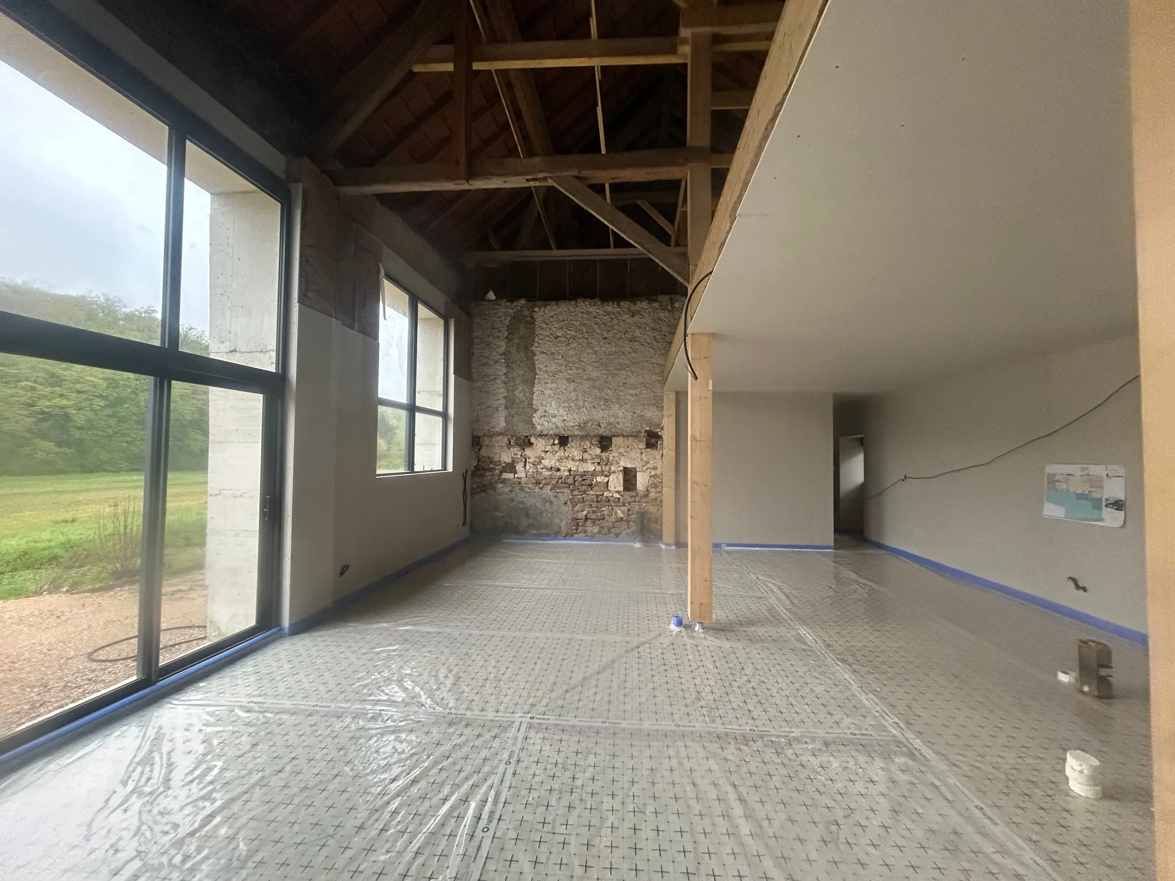 Grande pièce loft avec charpente bois apparente et pierre, avant chape — état après projection sol polyuréthane bâché · Pérouse · Isolatech