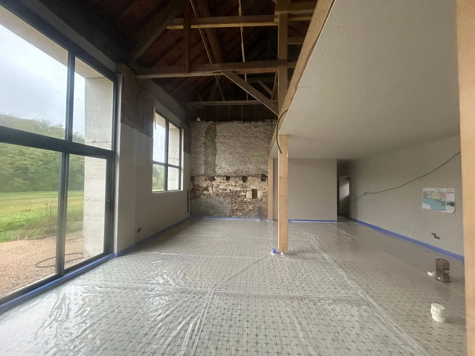 Grande pièce loft avec charpente bois apparente et pierre, avant chape — état après projection sol polyuréthane bâché · Pérouse · Isolatech