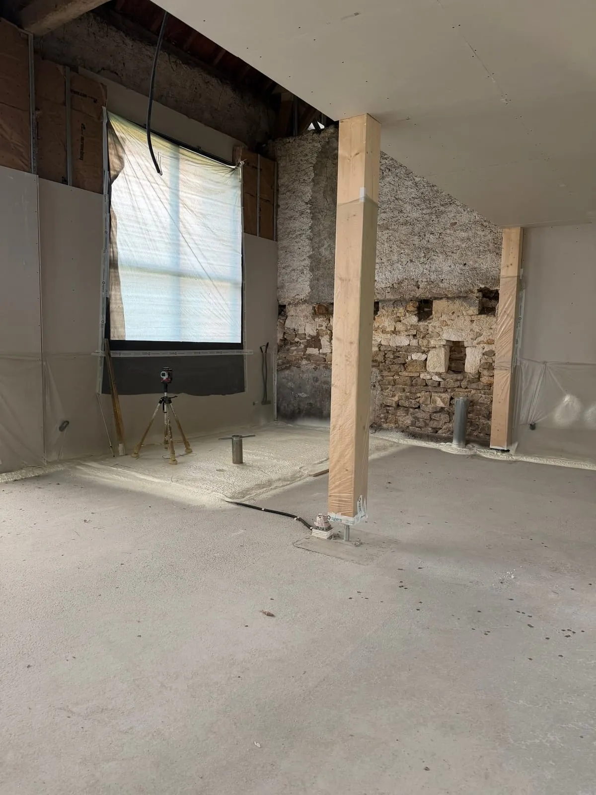 Pièce avec mur pierre apparente, poteaux bois et fenêtre en hauteur, état initial avant isolation des sols polyuréthane · Pérouse · Isolatech